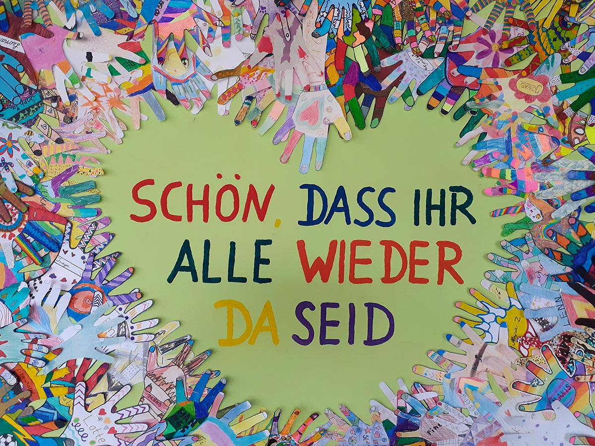Bunte Papierhände und die Aufschrift schön, dass ihr alle wieder da seid Bunte Papierhände und die Aufschrift schön, dass ihr alle wieder da seid